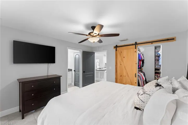 Bedroom with a spacious closet, a closet, ceiling fan, ensuite bathroom, and a barn door