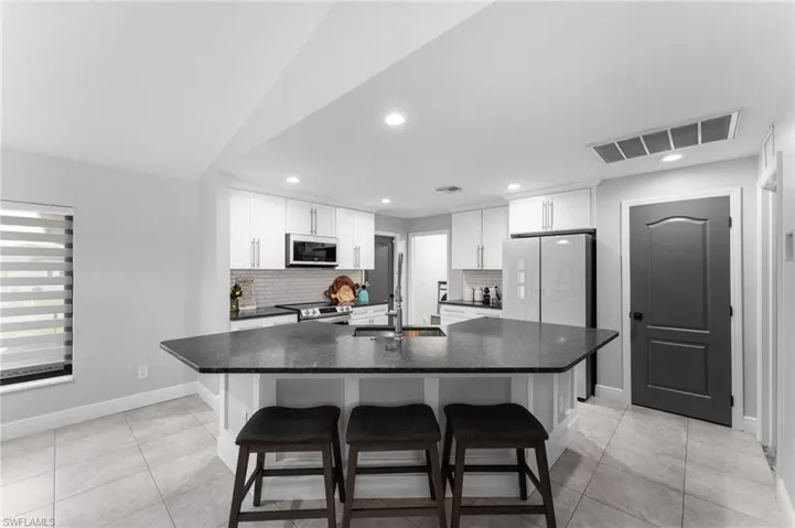 Kitchen featuring a kitchen breakfast bar, white appliances, white cabinets, and an island with sink