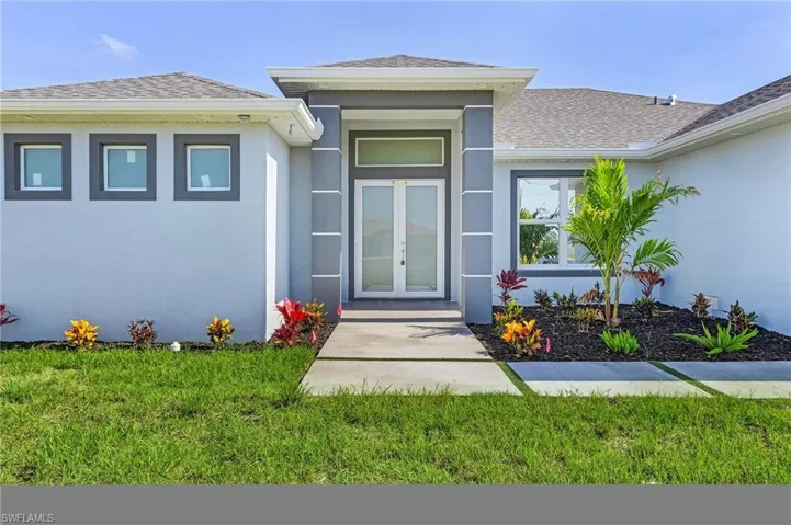 Doorway to property featuring a yard, a shingled roof, and stucco siding