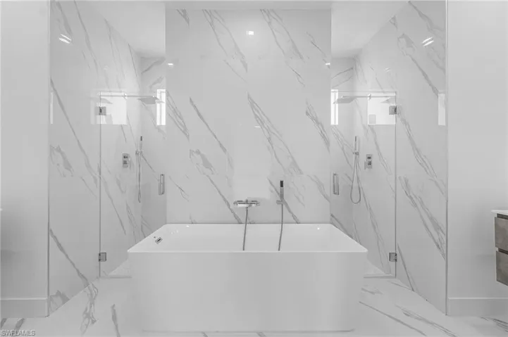 Full bath featuring marble tiled flooring, a marble finish shower, a freestanding tub, and stone wall