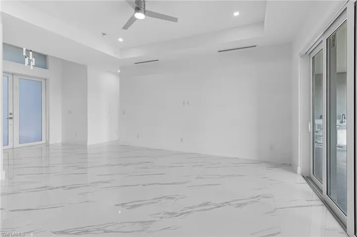 Empty room with french doors, light marble finish flooring, a tray ceiling, recessed lighting, and a ceiling fan
