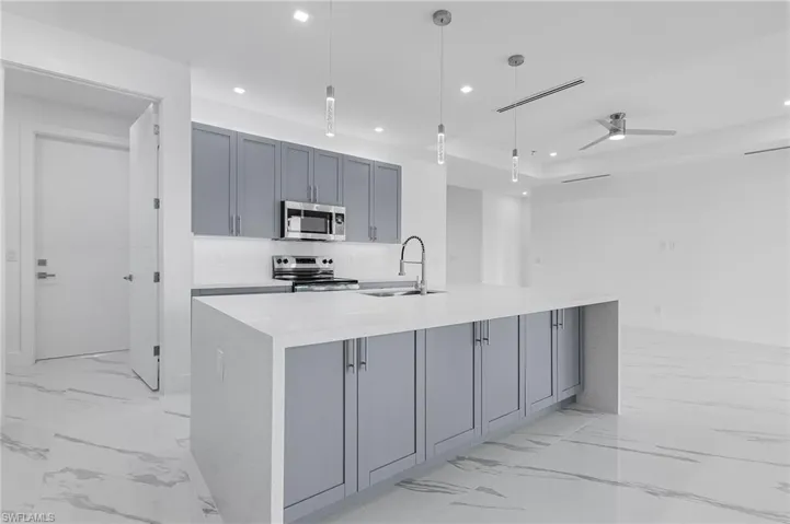 Kitchen with gray cabinets, light stone countertops, hanging light fixtures, appliances with stainless steel finishes, and light marble finish floors