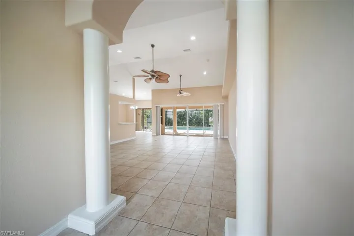 Corridor featuring light tile patterned floors, high vaulted ceiling, ornate columns, recessed lighting, and arched walkways