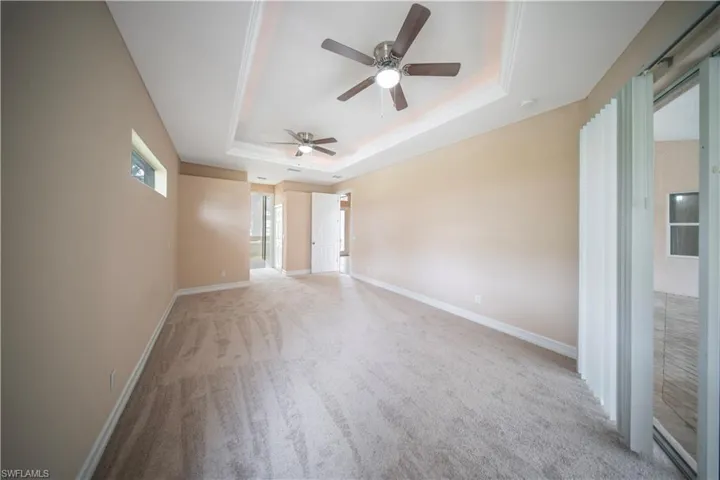 Spare room featuring a tray ceiling, light colored carpet, and a ceiling fan