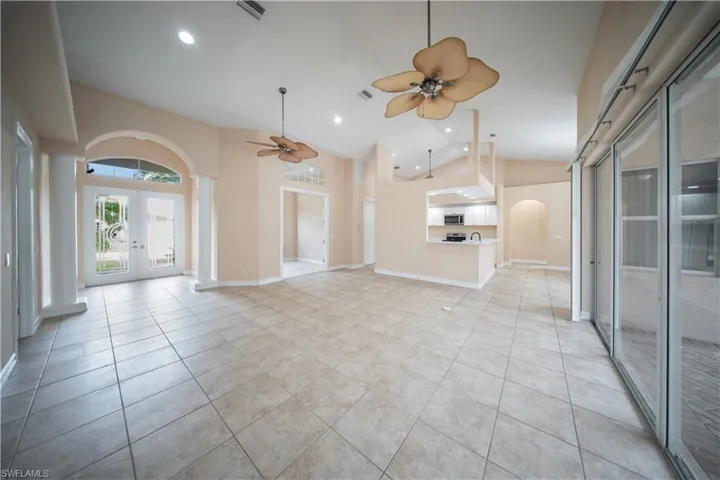 Unfurnished living room with arched walkways, light tile patterned floors, french doors, high vaulted ceiling, and recessed lighting