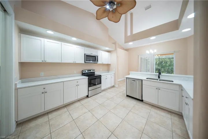 Kitchen featuring white cabinets, appliances with stainless steel finishes, light tile patterned flooring, recessed lighting, and lofted ceiling