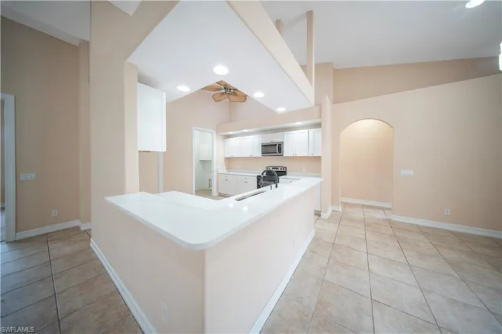 Kitchen with arched walkways, vaulted ceiling, white cabinetry, light tile patterned floors, and recessed lighting