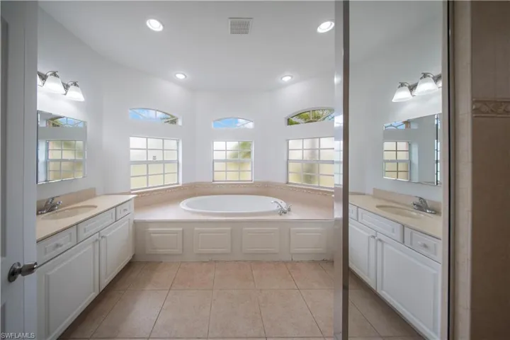 Full bathroom featuring two vanities, a bath, light tile patterned floors, and recessed lighting
