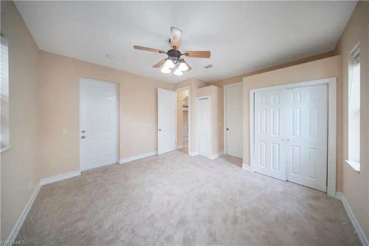 Unfurnished bedroom featuring multiple closets, light colored carpet, and a ceiling fan