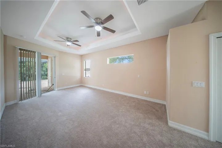 Empty room with a tray ceiling, carpet flooring, and a ceiling fan