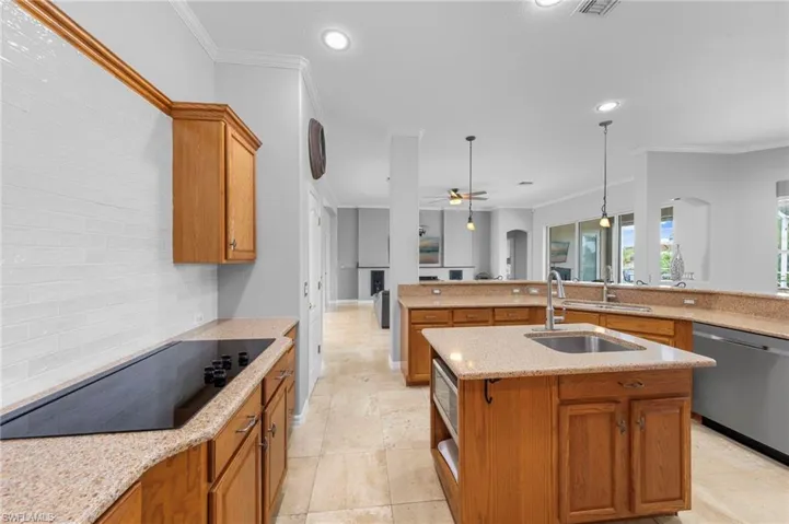 Kitchen featuring brown cabinets, crown molding, light stone countertops, hanging light fixtures, and black electric cooktop