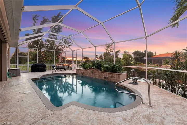 Pool at dusk with a sunroom, glass enclosure, an outdoor pool, and a patio area