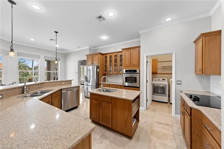 Kitchen with glass insert cabinets, decorative light fixtures, ornamental molding, brown cabinets, and backsplash
