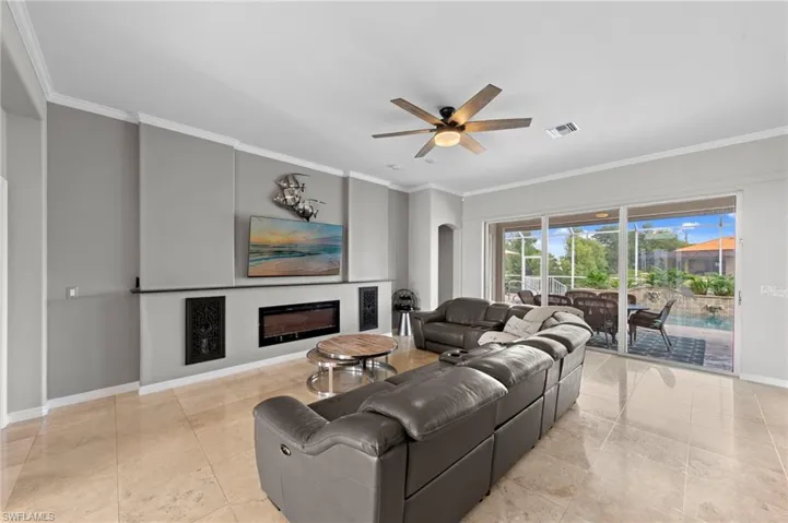 Living area featuring ornamental molding, a glass covered fireplace, a ceiling fan, and arched walkways