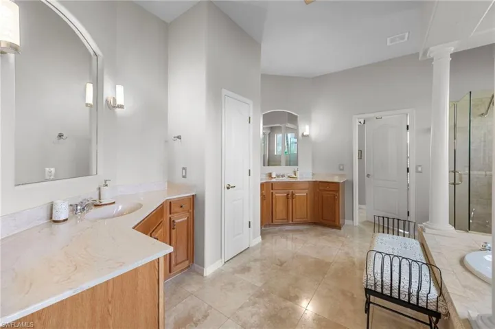 Bathroom with two vanities, a shower stall, light tile patterned floors, and decorative columns
