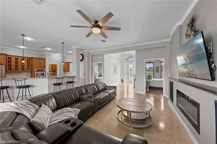 Living room featuring ornamental molding, light tile patterned floors, a ceiling fan, and a glass covered fireplace