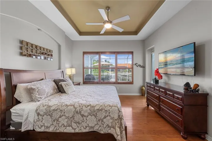 Bedroom with a raised ceiling, light wood-style flooring, and ceiling fan