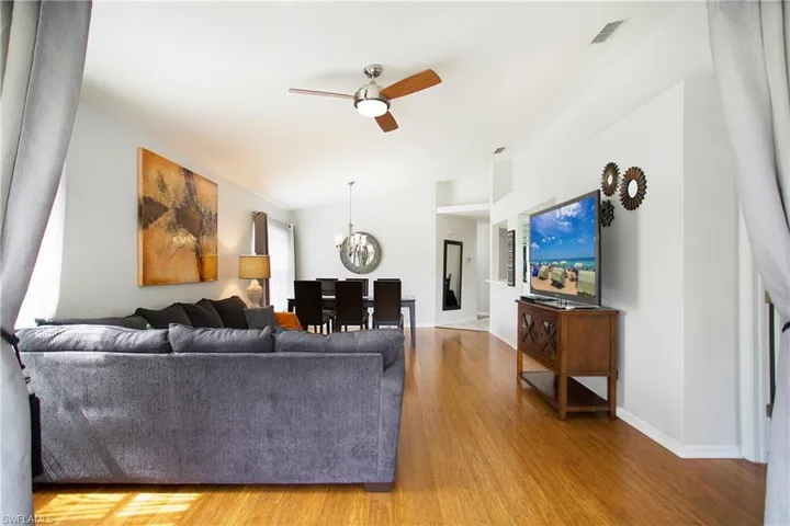 Living room featuring wood finished floors, ceiling fan, a chandelier, and lofted ceiling