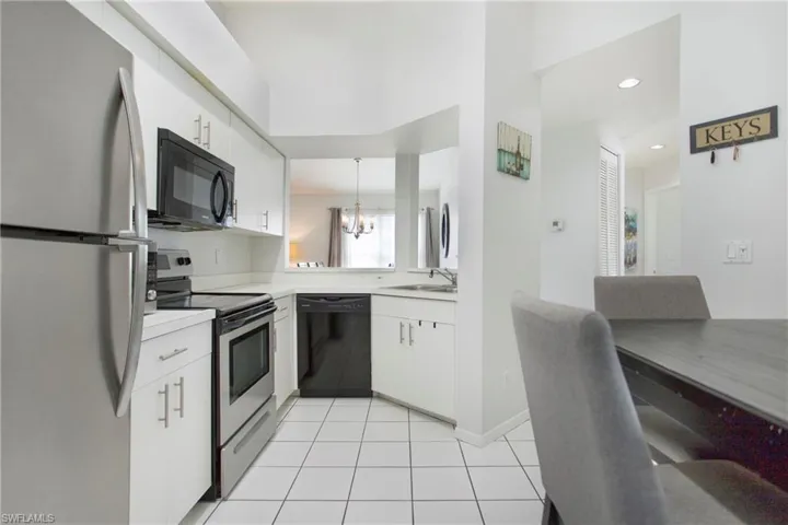 Kitchen with black appliances, light countertops, white cabinetry, a chandelier, and pendant lighting