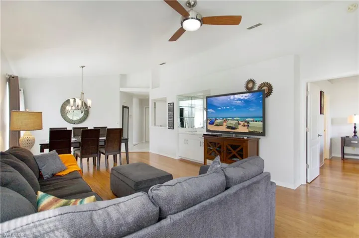 Living room featuring a chandelier, light wood-style flooring, ceiling fan, and vaulted ceiling