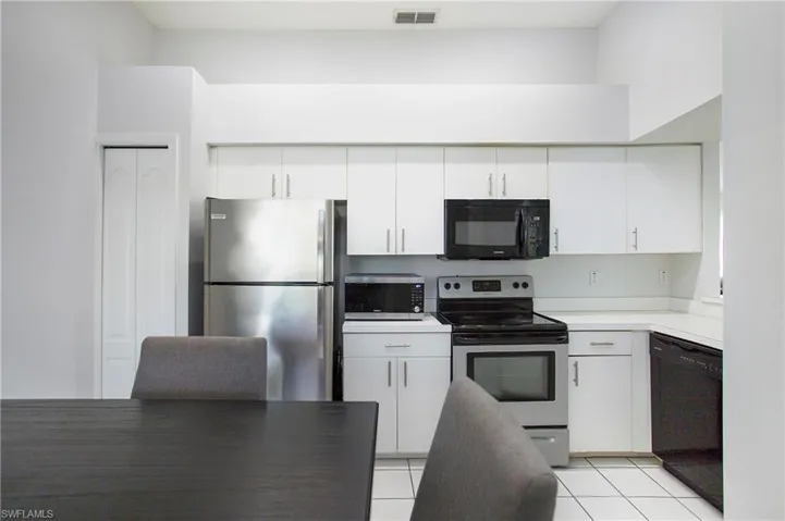 Kitchen with black appliances, light countertops, light tile patterned floors, and white cabinetry