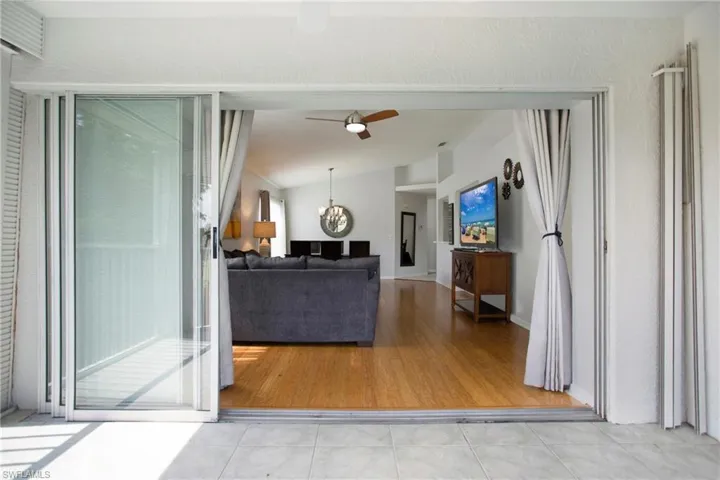 Living area with a chandelier, light tile patterned flooring, lofted ceiling, and ceiling fan