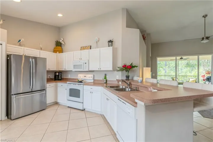 Kitchen featuring light tile flooring, ceiling fan, kitchen peninsula, and white appliances
