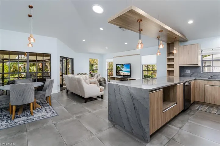 Kitchen featuring modern cabinets, dark stone counters, decorative backsplash, open floor plan, and light wood finish cabinets