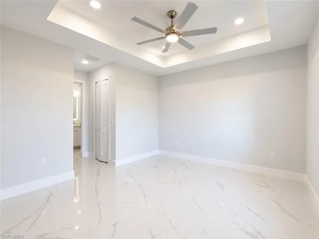 Spacious room featuring large format tile flooring, a tray ceiling with recessed lighting, a ceiling fan, and white baseboards
