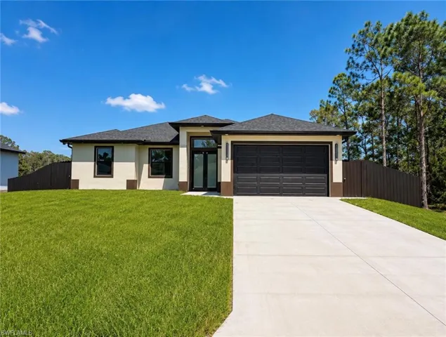 Contemporary stucco exterior with a dark shingle roof, integrated two-car garage, expansive concrete driveway, and a wooden privacy fence