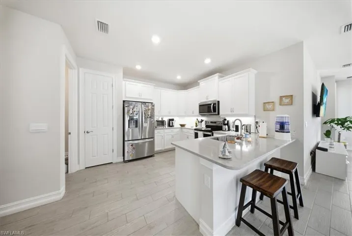 Kitchen featuring appliances with stainless steel finishes, a kitchen bar, white cabinets, a peninsula, and wood finish floors