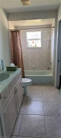 Full bath featuring vanity, shower / bath combo with shower curtain, and light tile patterned floors