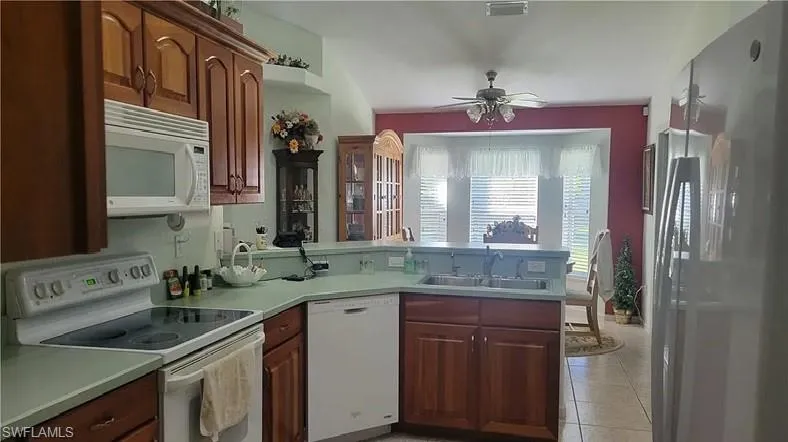 Kitchen featuring white appliances, a peninsula, a ceiling fan, light countertops, and light tile patterned floors