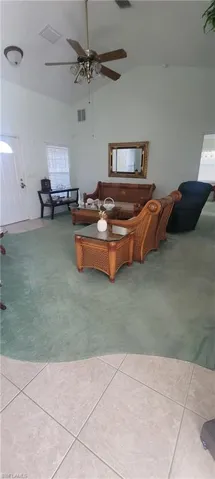 Living area with ceiling fan, lofted ceiling, light colored carpet, plenty of natural light, and light tile patterned flooring