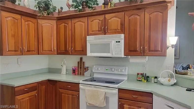 Kitchen with white appliances, light countertops, and wood finish cabinets