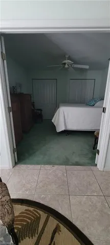 Bedroom with a closet, light colored carpet, a ceiling fan, and light tile patterned floors