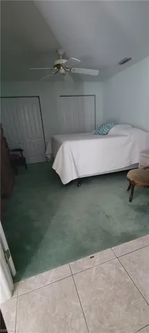 Bedroom featuring a ceiling fan, light tile patterned floors, light carpet, and two closets