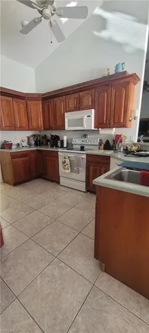 Kitchen featuring lofted ceiling, ceiling fan, white appliances, light countertops, and light tile patterned floors