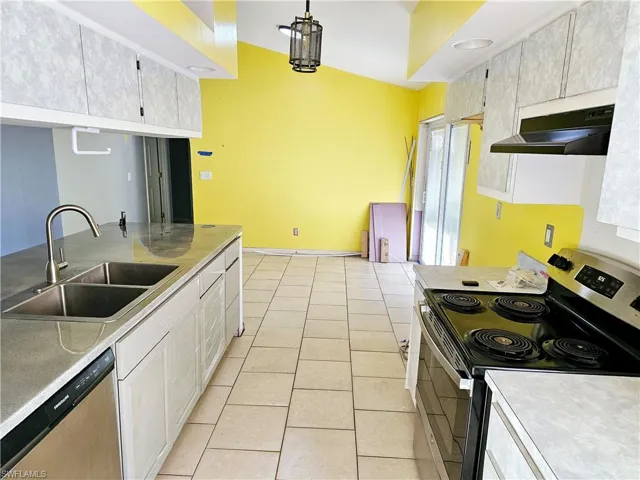 Kitchen featuring light tile patterned flooring, a sink, stainless steel appliances, light countertops, and under cabinet range hood