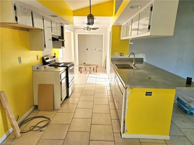 Kitchen with light tile patterned floors, a ceiling fan, a sink, vaulted ceiling, and electric stove