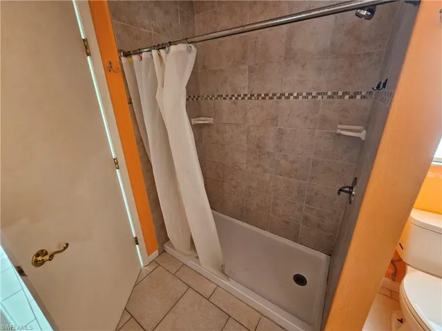 Full bathroom with a tile shower, tile patterned flooring, and toilet