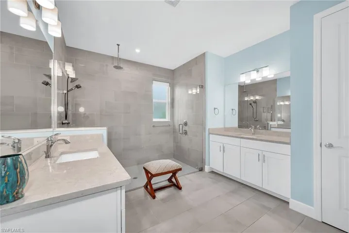 Expansive bathroom featuring dual vanity sinks set in light-toned countertops, a spacious walk-in shower with full-height gray tile, and a rainfall showerhead