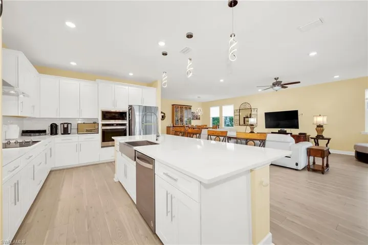 Open concept kitchen featuring an expansive island with a farmhouse sink, white shaker cabinetry, stainless steel appliances, and light wood-finish flooring