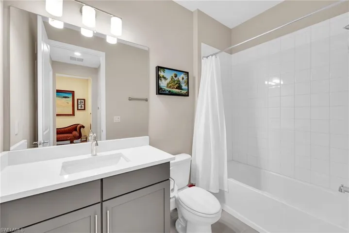 Bathroom featuring a white rectangular undermount sink, a gray vanity with double-door cabinetry, a white countertop, and a built-in bathtub with white subway tile surround
