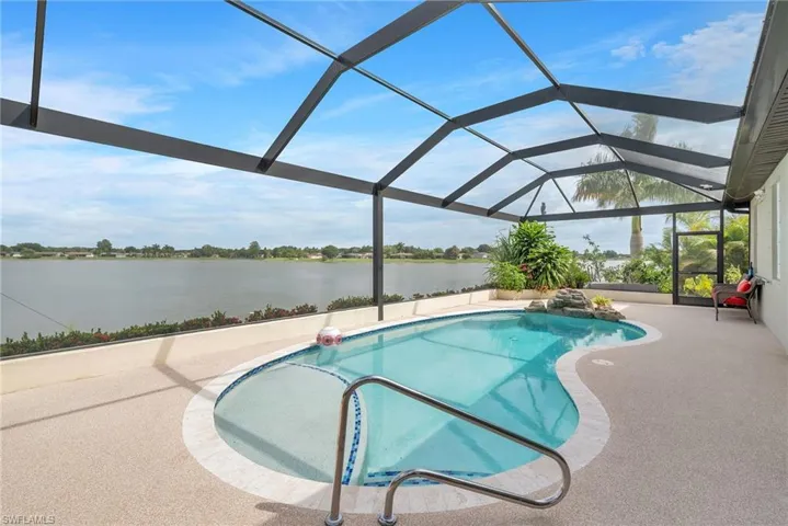 Screened-in pool deck featuring a freeform pool with integrated waterfall feature, water frontage, and surrounding tropical landscaping