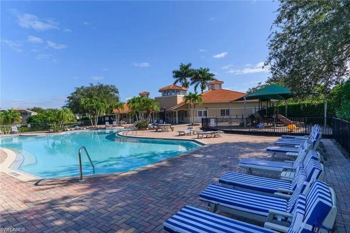 Expansive pool area featuring a large, blue-tiled swimming pool and surrounding paver decking
