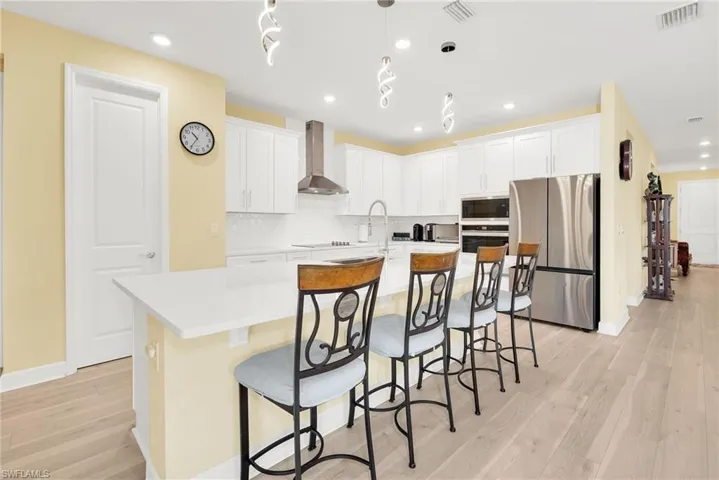 Kitchen featuring an expansive island with a white countertop, white shaker cabinetry, stainless steel appliances, a white subway tile backsplash, and light wood-finish flooring