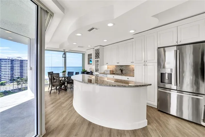 Kitchen with white cabinets, dark stone countertops, stainless steel fridge with ice dispenser, visible vents, and light wood-style floors
