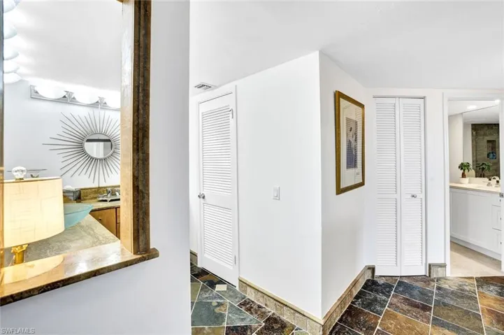 Hallway featuring stone tile floors, baseboards, a sink, and visible vents