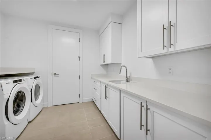 Laundry area with cabinets, separate washer and dryer, sink, and light tile patterned floors